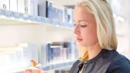 Blonde Frau mit Parfumflakon in der Hand vor einem Regal mit Kosmetikprodukten.
