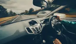 Widok z wnętrza samochodu podczas jazdy po drodze, z ręką na kierownicy.