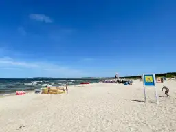 Słoneczna plaża Cztery Wiatry z piaskiem, morzem i ludźmi. W oddali widać ratownika na wieży.