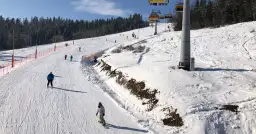 Narciarze i snowboardziści na ośnieżonym stoku z wyciągiem krzesełkowym w tle.