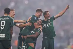 Piłkarze w zielonych koszulkach świętują zwycięstwo, jeden z nich jest podnoszony przez kolegów.