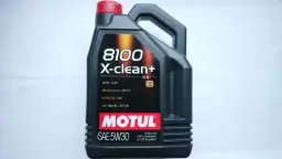 Czarna bańka oleju silnikowego Motul 8100 X-clean+ 5W30 na białym tle.