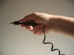 Dłoń trzymająca czarny kabel z wtyczką.