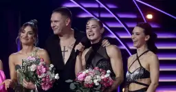 Uśmiechnięci ludzie na scenie z bukietami kwiatów.
