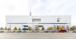 Nowoczesny, biały budynek muzeum w Warszawie z czerwonym autobusem i samochodami na ulicy.