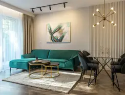 Jasne zasłony i beżowe firanki idealnie komponują się z zieloną kanapą, tworząc przytulną atmosferę.