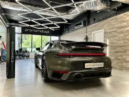 Ciemnozielone Porsche 911 w garażu z nowoczesnym oświetleniem i stojącym obok pionowym banerem.