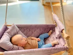 Niemowlę leżące w fioletowej huśtawce z poduszką.