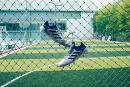 Stylowe buty piłkarskie wiszące na siatce, gotowe na mecz na orliku.