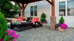 Jak zbudować taras? Wygodny zestaw wypoczynkowy, stolik i piękne kwiaty na wybrukowanym patio.