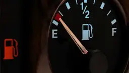 Wskaźnik paliwa w Toyocie Yaris pokazuje niski poziom. Czerwona lampka ostrzegawcza z ikoną dystrybutora paliwa świeci się, a wskazówka na wskaźniku znajduje się blisko litery "E", sygnalizując niski **pojemność baku**.