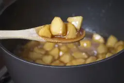 Kawałki jabłek gotujące się w syropie na łyżce, idealne, by pokazać, jak zagęścić jabłka do szarlotki budyniem.