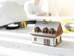 Model domu na planach, kask budowlany i poziomica. Zastanawiasz się, ile kosztuje budowa garażu?