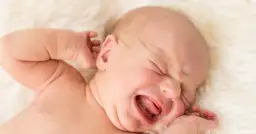 Noworodek z otwartymi ustami i zamkniętymi oczami, leżący na białym futerku.