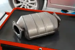 Metalowy katalizator samochodowy leżący na czarnej powierzchni.