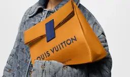Pomarańczowa torba Louis Vuitton z granatowym logo, trzymana na tle dżinsowej kurtki z monogramem.