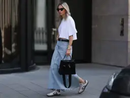 Kobieta w białej bluzce i długiej jeansowej spódnicy, z czarną torebką. Inspiracja: co nosić do jeansowej spódnicy.