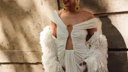 Elegancka sesja fashion: modelka w kremowej sukni z wycięciem i futrzanym bolerkiem, ozdobiona złotą biżuterią.