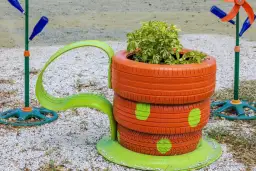 Stos opon pomalowanych na pomarańczowo z zielonymi kropkami, tworzący doniczkę z rośliną.