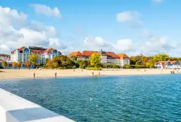 Piękna miejscowość nad morzem na S. Hotel z czerwonym dachem i plaża z kilkoma spacerującymi ludźmi.