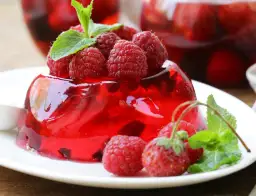 Czerwona galaretka z malinami i listkami mięty na białym talerzu.