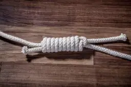 Zbliżenie na węzeł łączący dwie białe liny na drewnianym tle.