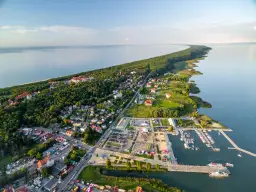 Widok z lotu ptaka na Krynicę Morską. Widać zalew, lasy, zabudowania i tętniący życiem rynek z mariną pełną łodzi.