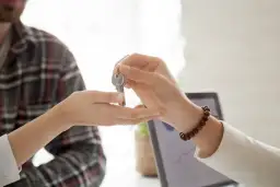 Przekazywanie kluczy do lokalu, w tle laptop z wykresem.