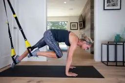 Kobieta wykonuje ćwiczenie z taśmami TRX, angażując mięśnie brzucha i nóg. Intensywny trening TRX w domowym zaciszu.