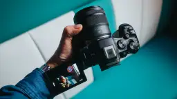 Dłoń trzyma zaawansowany **canon aparat lustrzanka** z obiektywem RF 45mm. Na ekranie widoczny jest podgląd ujęcia.