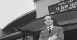 Jean Pierre Léaud w garniturze, z rękami skrzyżowanymi na piersi, przed budynkiem z napisem "Le Beau Serge".