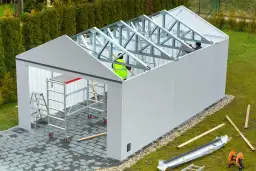 Budowa garażu w toku. Pracownicy montują konstrukcję dachu. Czy na budowę garażu potrzebne jest pozwolenie? To pytanie nurtuje wielu inwestorów.