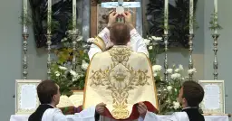 Kapłan podnosi hostię do krzyża. To nie jest czarna msza, lecz uroczysta msza święta.