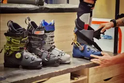 Kilka par butów narciarskich w różnych kolorach i markach, jedna para jest zakładana.