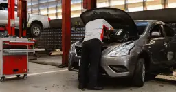 Mechanik naprawia samochód z otwartą maską w warsztacie.