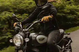 Motocyklista w kasku i rękawiczkach jedzie motocyklem. W tle zielony las. To świetny moment, by nauczyć się, jak zmieniać biegi w motorze.