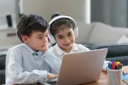 Dzieci uczą się, jak otworzyć YT w przeglądarce, korzystając z laptopa. Dziewczynka ma słuchawki.