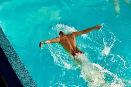 Pływak w czerwonych kąpielówkach wykonuje motylka, najszybszy styl pływacki, rozbijając wodę.