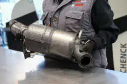 Mechanik w rękawiczkach trzyma metalowy element układu wydechowego samochodu.