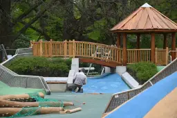 Budowa placu zabaw w Parku Ujazdowskim: drewniana altana, mostek, zjeżdżalnie i pracownik.