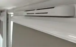 Biały nawiewnik okienny z logo "Aira HY". Dowiedz się, jak zamknąć wywietrzniki w oknach, aby zapewnić komfort termiczny.