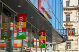 Baner mBank z kolorowym logo i napisem "mBank" na tle nowoczesnego budynku.