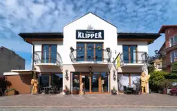 Tawerna "Klipper" we Władysławowie z drewnianymi rzeźbami i stolikami na zewnątrz.