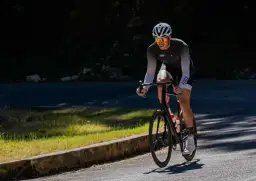 Kolarz w kasku i okularach przeciwsłonecznych pedałuje pod górę. Czy jazda na rowerze wzmacnia mięsień czworogłowy? Ten sport na pewno angażuje nogi.