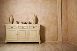 Elegancka komoda z crackle na drzwiach, inspirowana glinką wenecką, na tle ściany o ciepłej, rustykalnej fakturze.