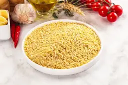 Miseczka pełna makaronu orzo, idealnego do przygotowania pysznego dania. Obok czosnek, papryczki chili, pomidorki i oliwa.