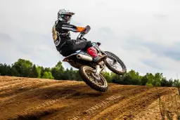 Motocyklista w kasku i kombinezonie skacze na motocyklu po piaszczystym torze.