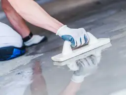 Ręka w rękawicy wygładza mokrą wylewkę. Czas, ile schnie wylewka, zależy od wielu czynników.