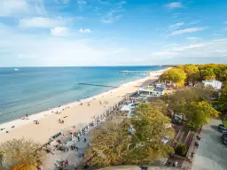 Słoneczny deptak w Kołobrzegu tętni życiem. Ludzie spacerują po plaży i promenadzie, ciesząc się jesiennym słońcem i widokiem na morze.