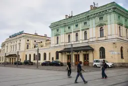 Kraków Główny. Krótki spacer z dworca na rynek, przez plac przed zabytkowym budynkiem, gdzie przechodzą ludzie.